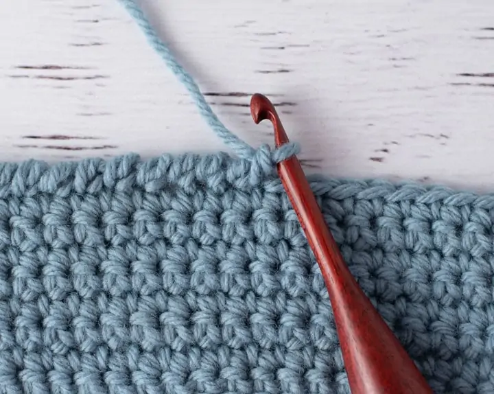 blue crochet piece and wood crochet hook, demonstrating reverse single crochet stitch