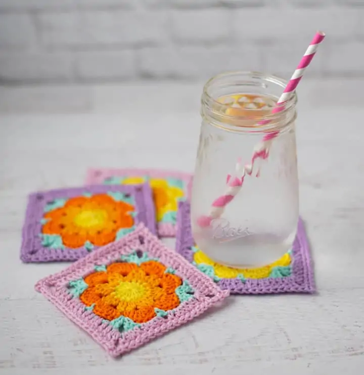 iced water on purple, pink, A glass of water on gold and orange crochet flower coasters