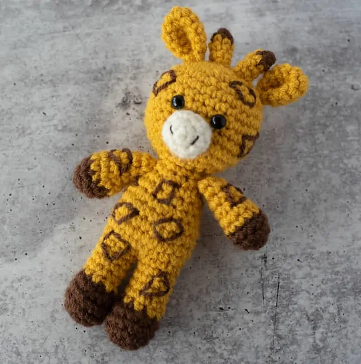 yellow and brown crochet stuffed giraffe on a gray cement background