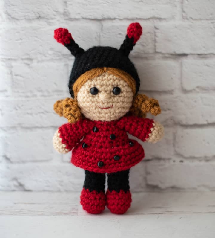 crochet doll with gold hair dressed up as a ladybug with a black hat