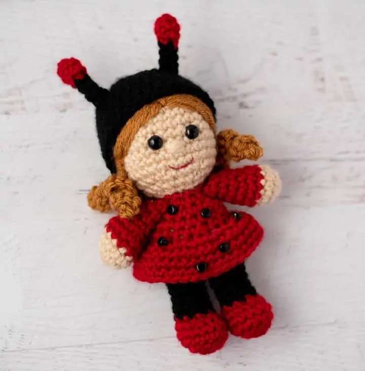 crochet doll with gold hair dressed up as a ladybug with a black hat