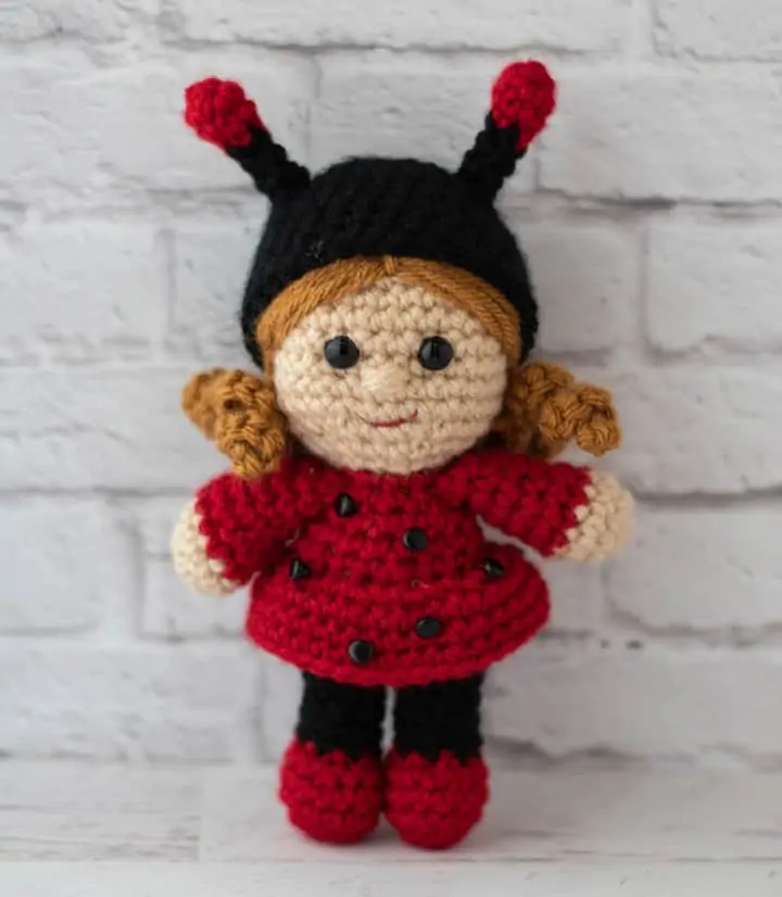 crochet doll with gold hair dressed up as a ladybug with a black hat