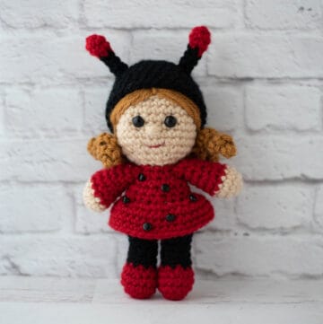 crochet doll with gold hair dressed up as a ladybug with a black hat