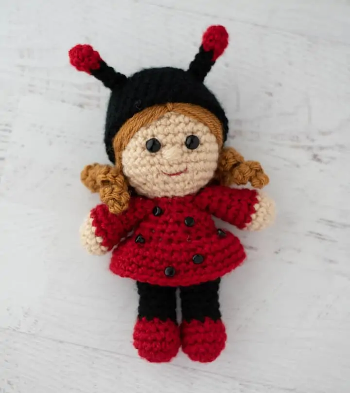 crochet doll with gold hair dressed up as a ladybug with a black hat