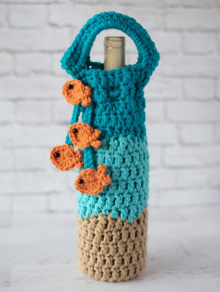 crochet wine cozy in blue, light brown with a blue tie with gold fish