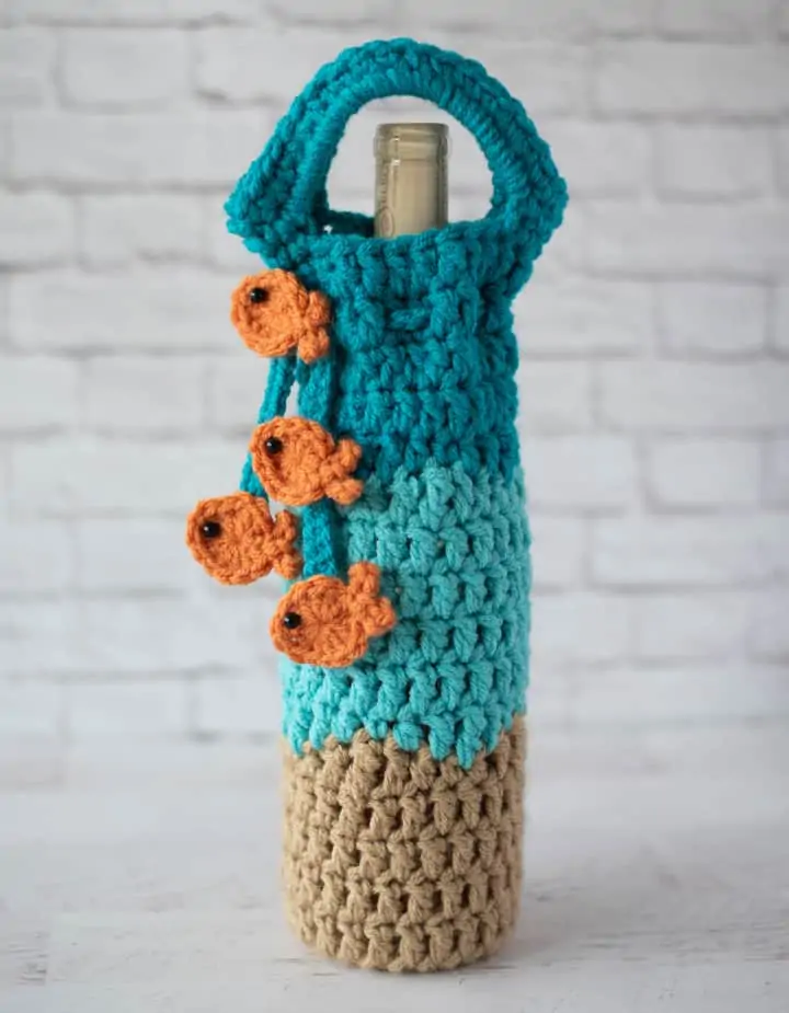 crochet wine cozy in blue, light brown with a blue tie with gold fish