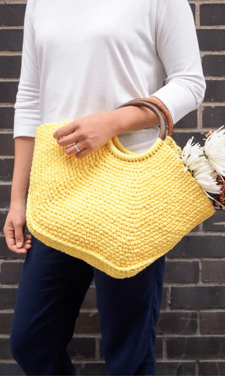 woman holding yellow crochet bag with flowers in it