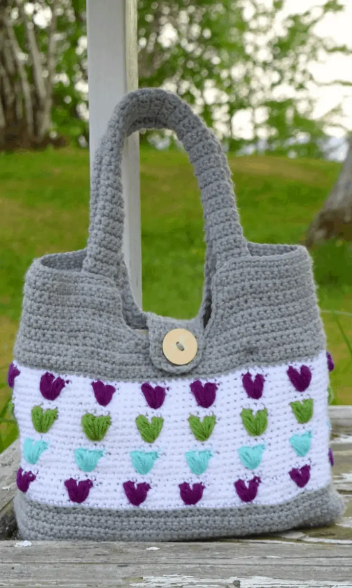 grey and white crochet bag with purple and green hearts on it