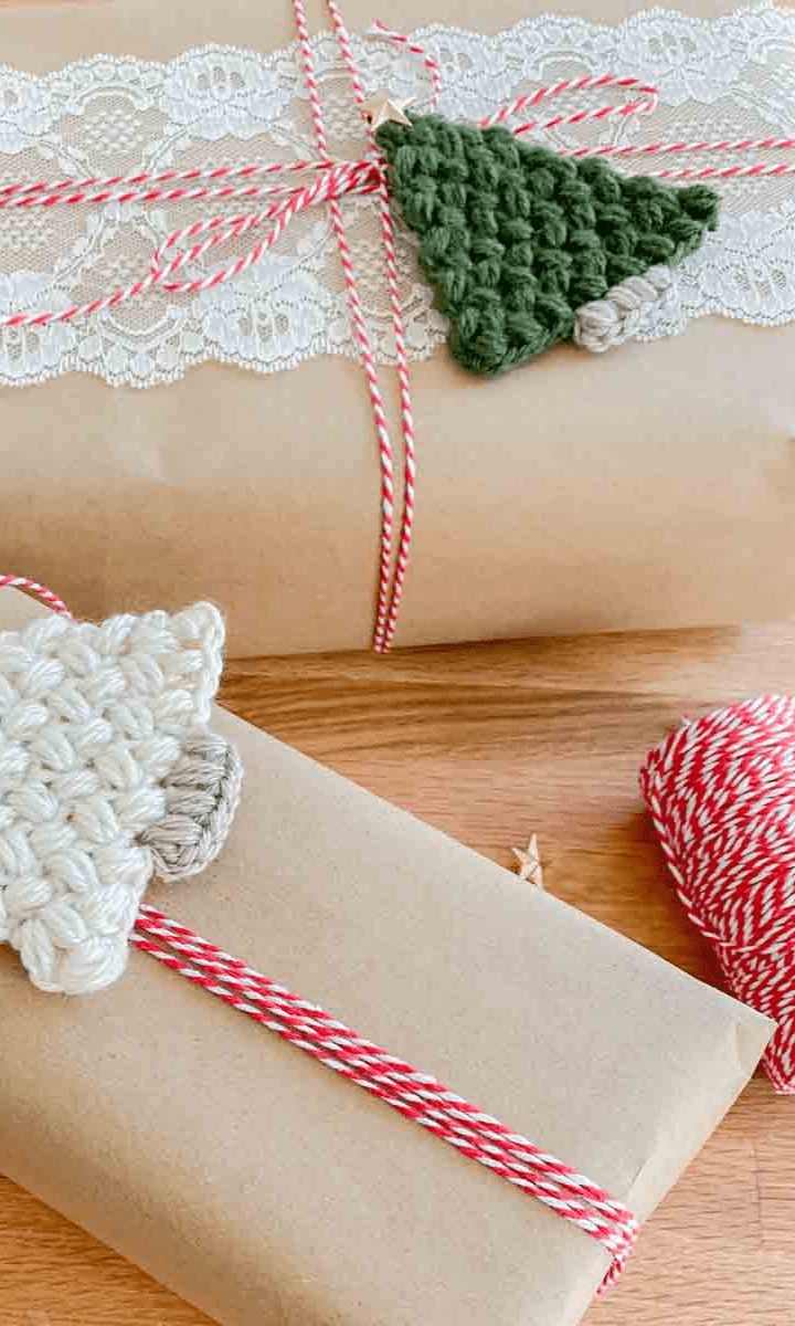 two flat crochet christmas trees, one white and one green, attached to two brown packages