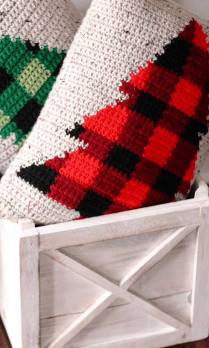two white crochet pillows in a basket with plaid christmas trees