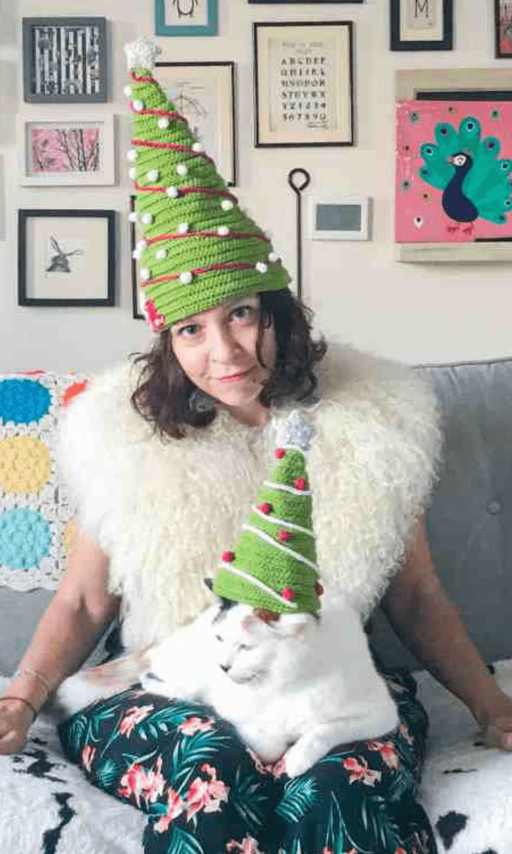 lady with christmas tree hat sitting on couch with cat with christmas tree hat