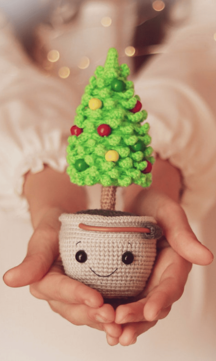 person holding a crochet christmas tree amigurumi in crochet flower pot