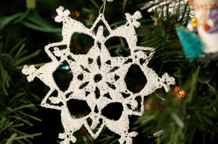 white crochet snowflake ornament hanging on christmas tree