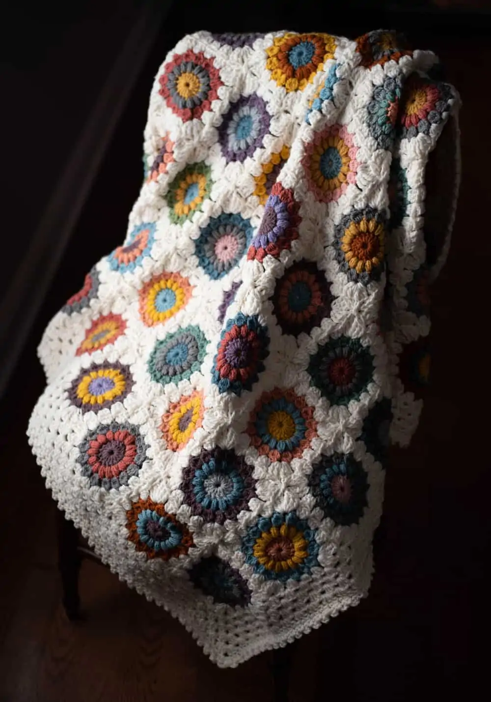 Crochet multi color afghan with ivory border on a chair