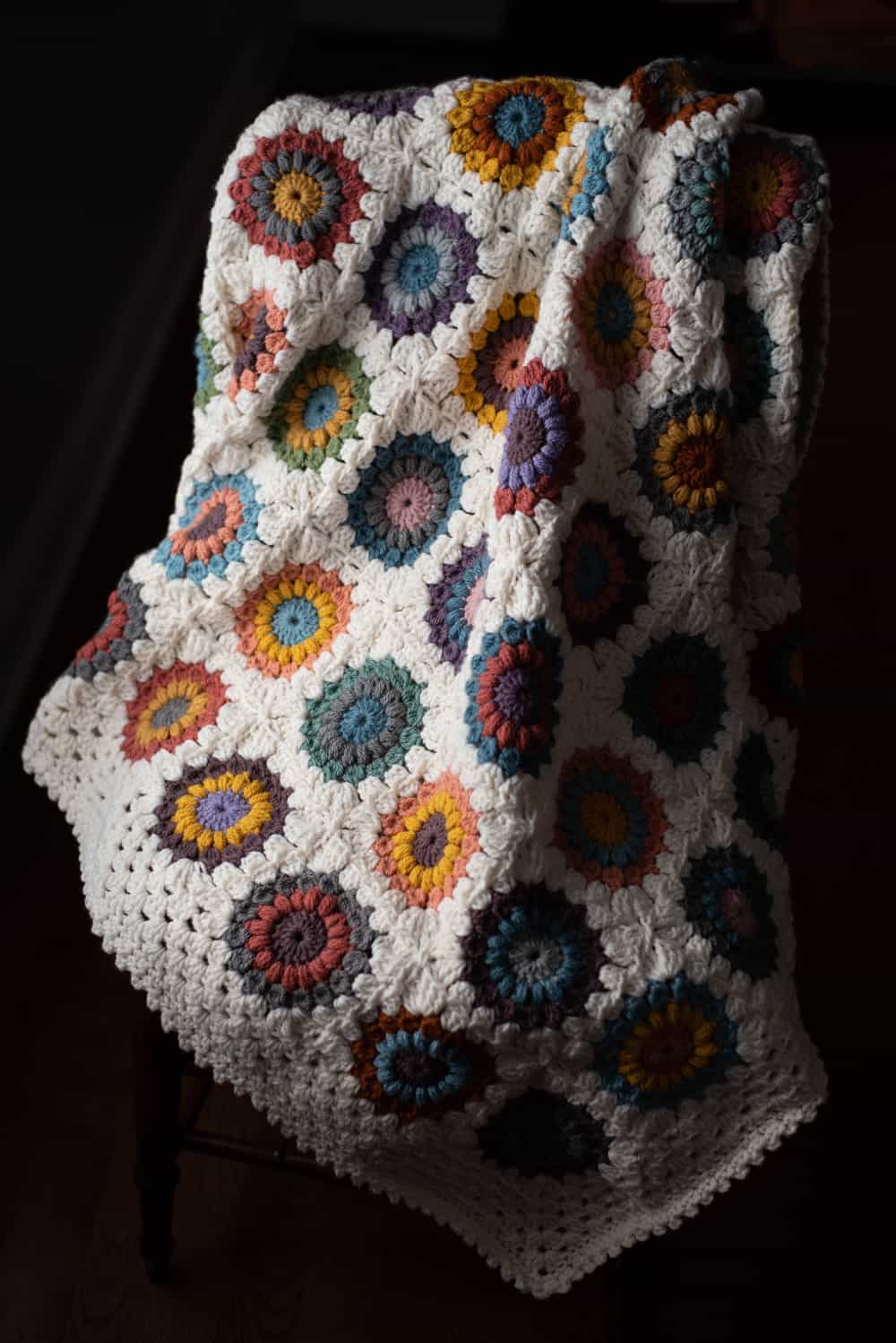 Crochet multi color afghan with ivory border on a chair