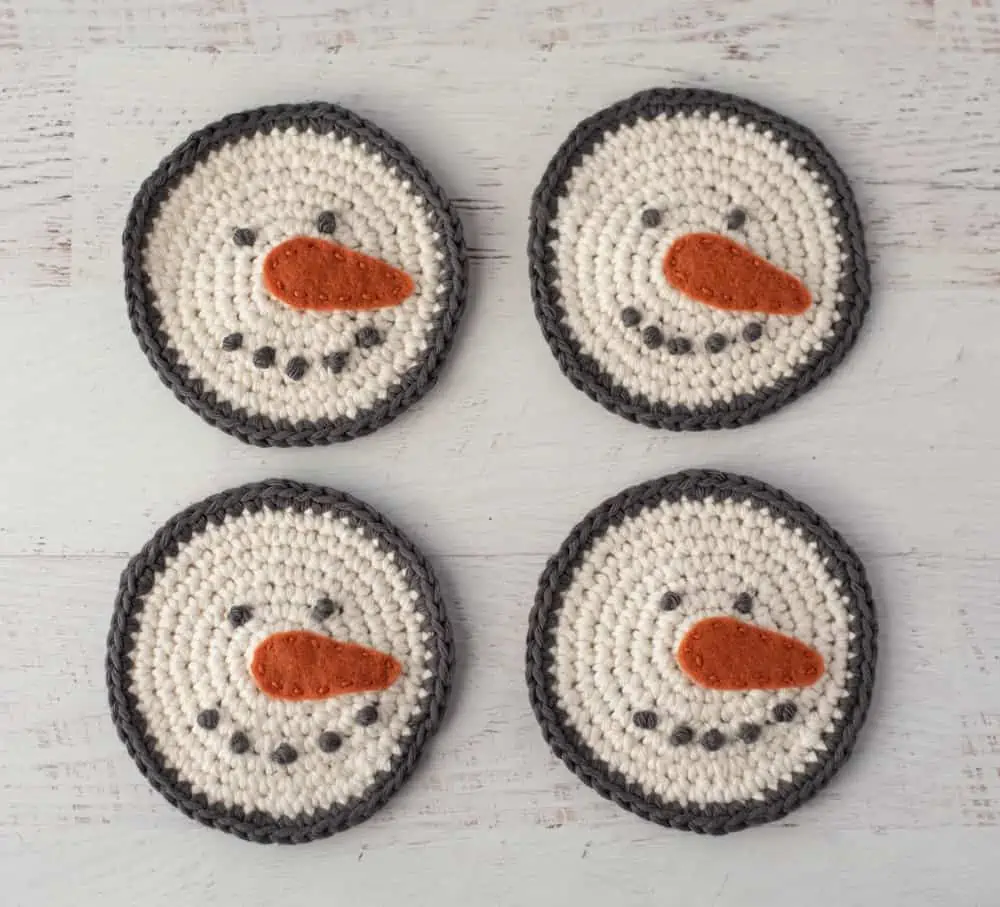 Four cream and gray crochet snowman coasters with orange carrot nose