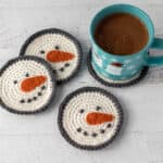 cream and gray crochet snowman coasters with orange carrot nose with cup of hot cocoa
