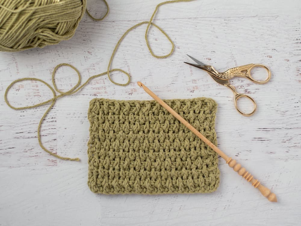 Crochet rice stitch sample in green yarn with wood hook and stork scissors