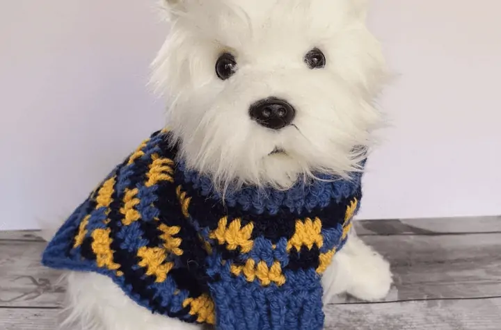 A toy dog wearing a blue and yellow heckered dog sweater.