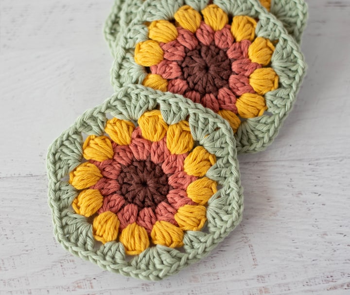 crochet sunflower coasters in brown, orange, yellow and green yarn