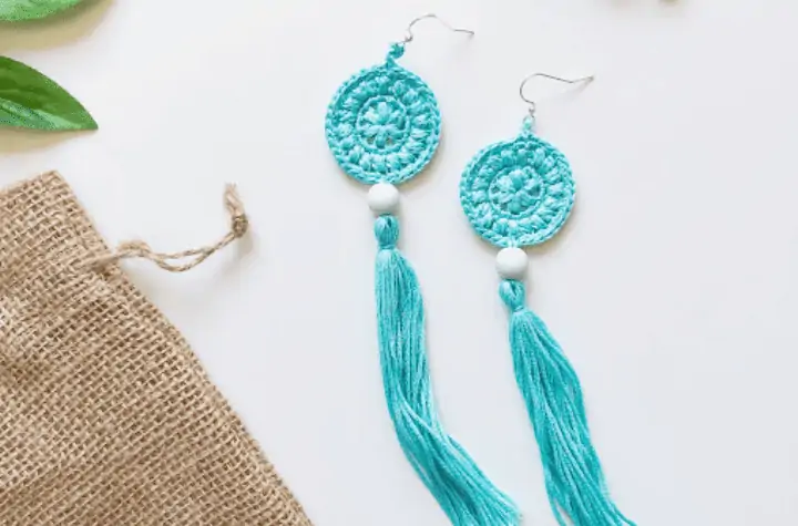 Blue crochet earrings that have a circle at the top with a long tassel on the bottom.