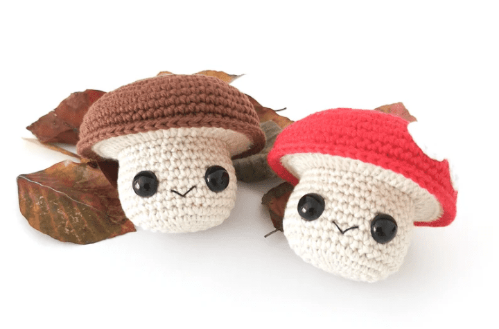 Two little mushroom amigurumis, one with a red cap and one with a brown cap.