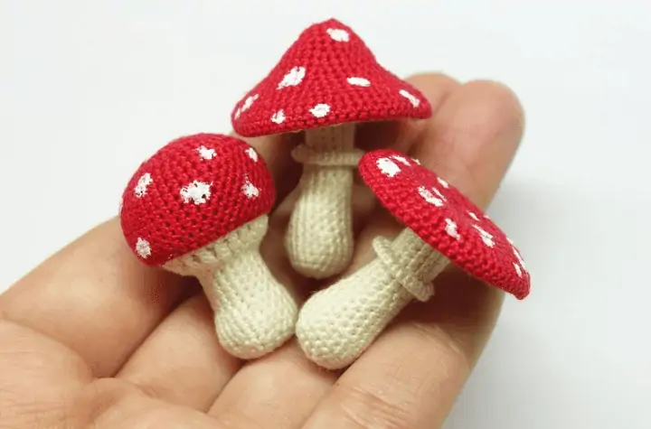 Very small crochet mushroom toadstools in the palm of someone's hand