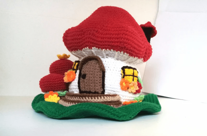 Maison champignon au crochet avec un fond vert qui ressemble à de l'herbe.