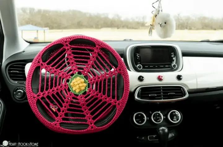A spider-web style crochet steering wheel cover with a flower in the middle.