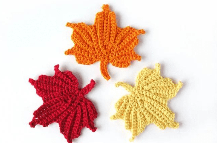 A crochet maple leaf in orange, red, and off white.