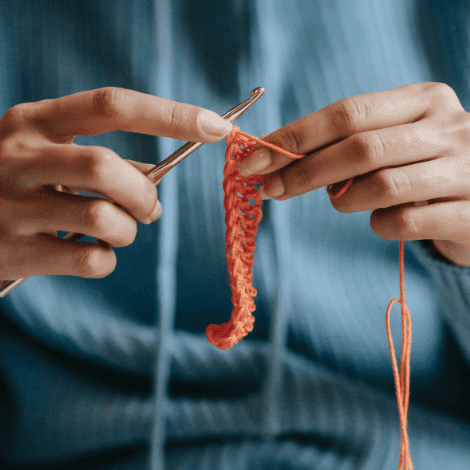 woman crocheting with orange yarn