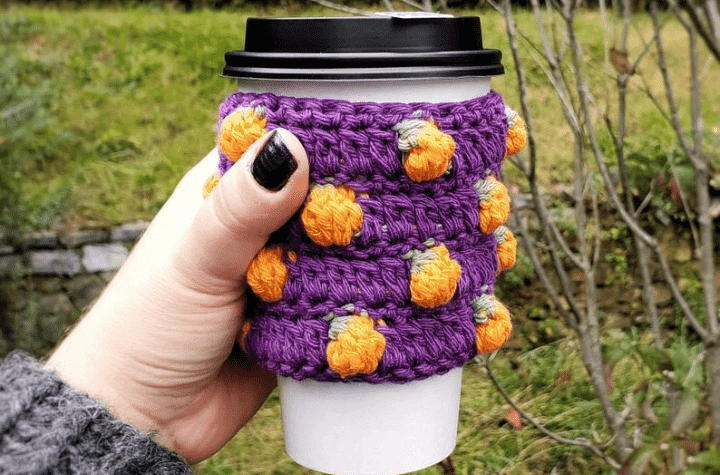 Cup cozy with a purple background and a bunch of small pumpkins.