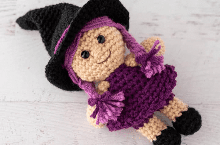 Witch amigurumi pattern with a purple dress and purple braids.