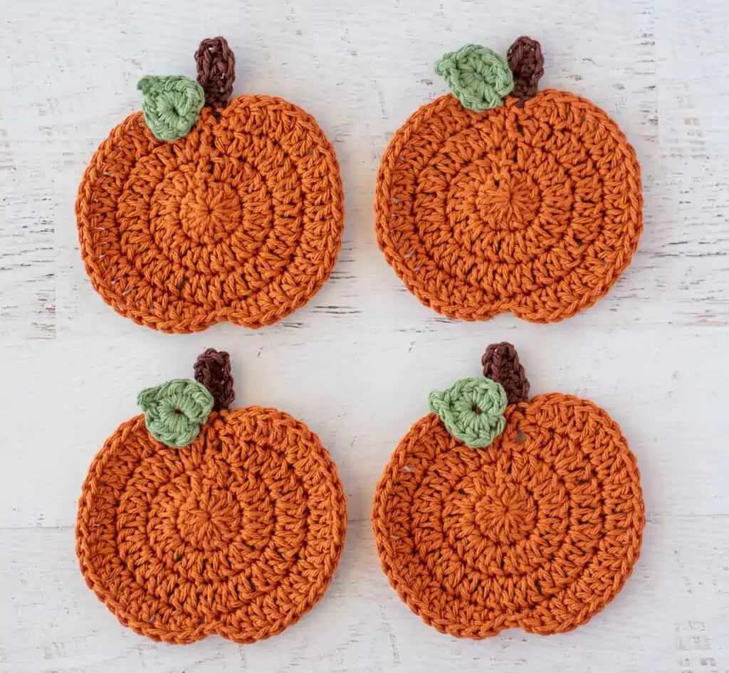 4 crochet orange pumpkins each with a brown stem and one green leaf