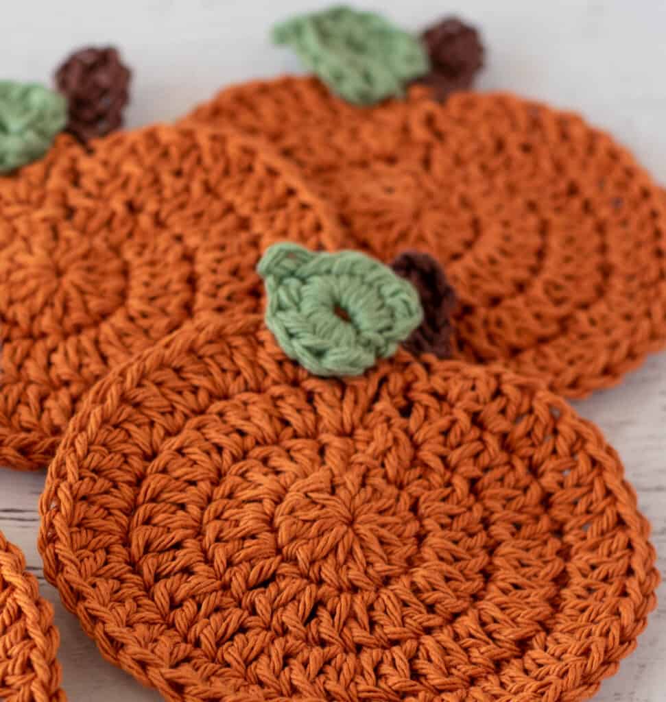 Up close view of orange crochet pumpkin coasters with brown stems and green leaves