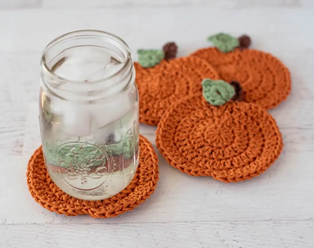 orange crochet pumpkin coasters with glass of ice water