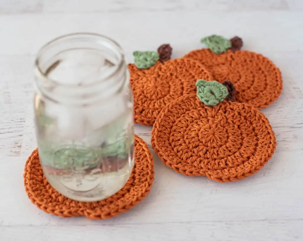 Orange crochet pumpkin coasters with glass of ice water