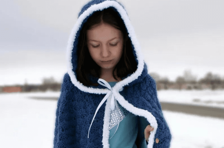 A child wearing a blu crocheted cloak with a hood.