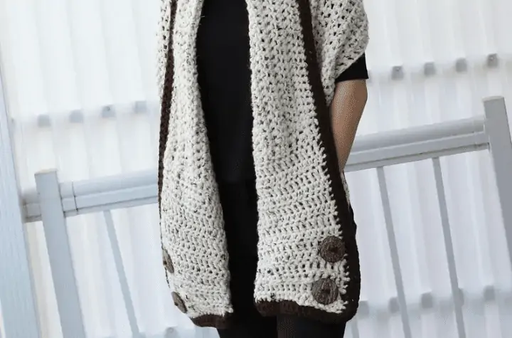 Crochet shawl with a brown border and four large buttons on the pockets.