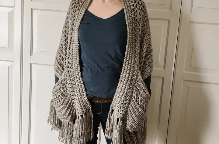 Beige crochet shawl with pockets and fringe along the bottom.