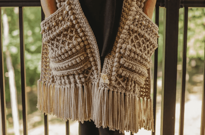 Crochet pocket shawl that uses a variety of specialized stitches and features fringe along the bottom.