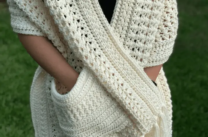 White crochet pocket shawl with fringe along the bottom.