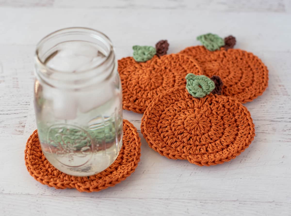 Orange crochet pumpkin coasters with glass of ice water