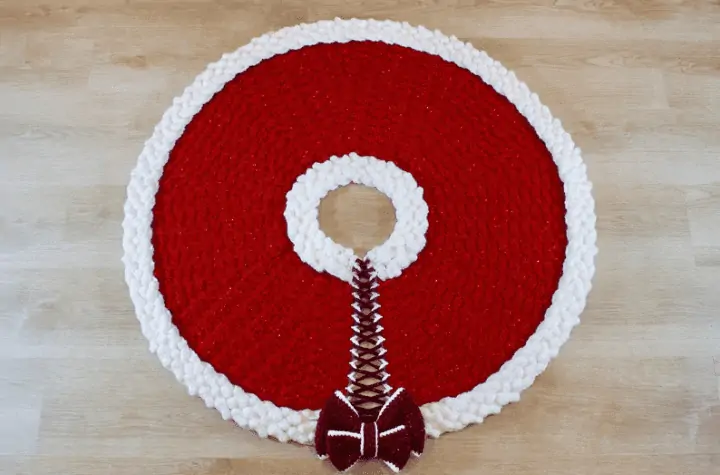 Mostly red tree skirt with white edges and it fatened together with a bow.