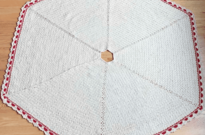 A mostly white tree skirt featuring red detailing along the edges.