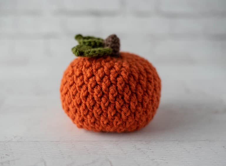 Orange crochet textured pumpkin with brown stem and green leaves