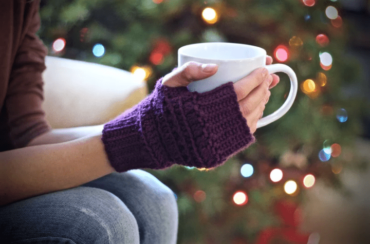 Person wearing purple fingerless gloves, holding a coffee mug.