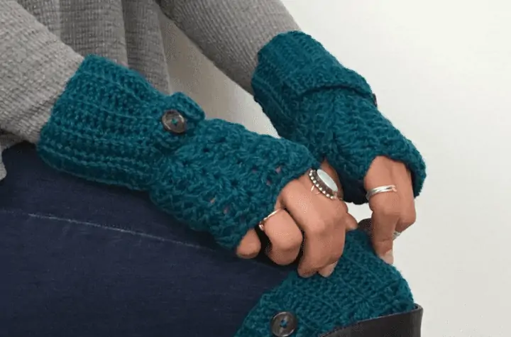 Blue crochet gingerless gloves with a decorative button by the wrist.