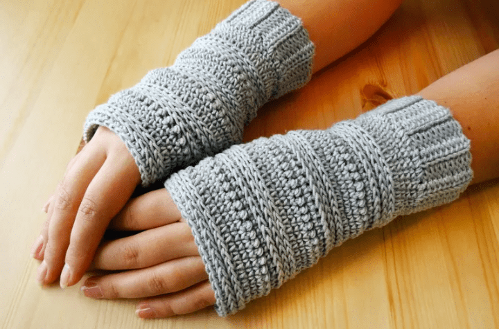 Grey crochet fingerless gloves that feature a variety of different stitches.