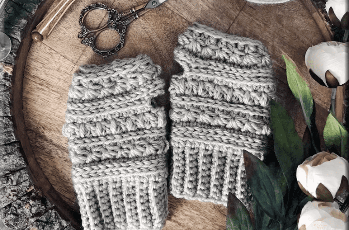 Grey crochet fingerless gloves on a wooden backdrop.